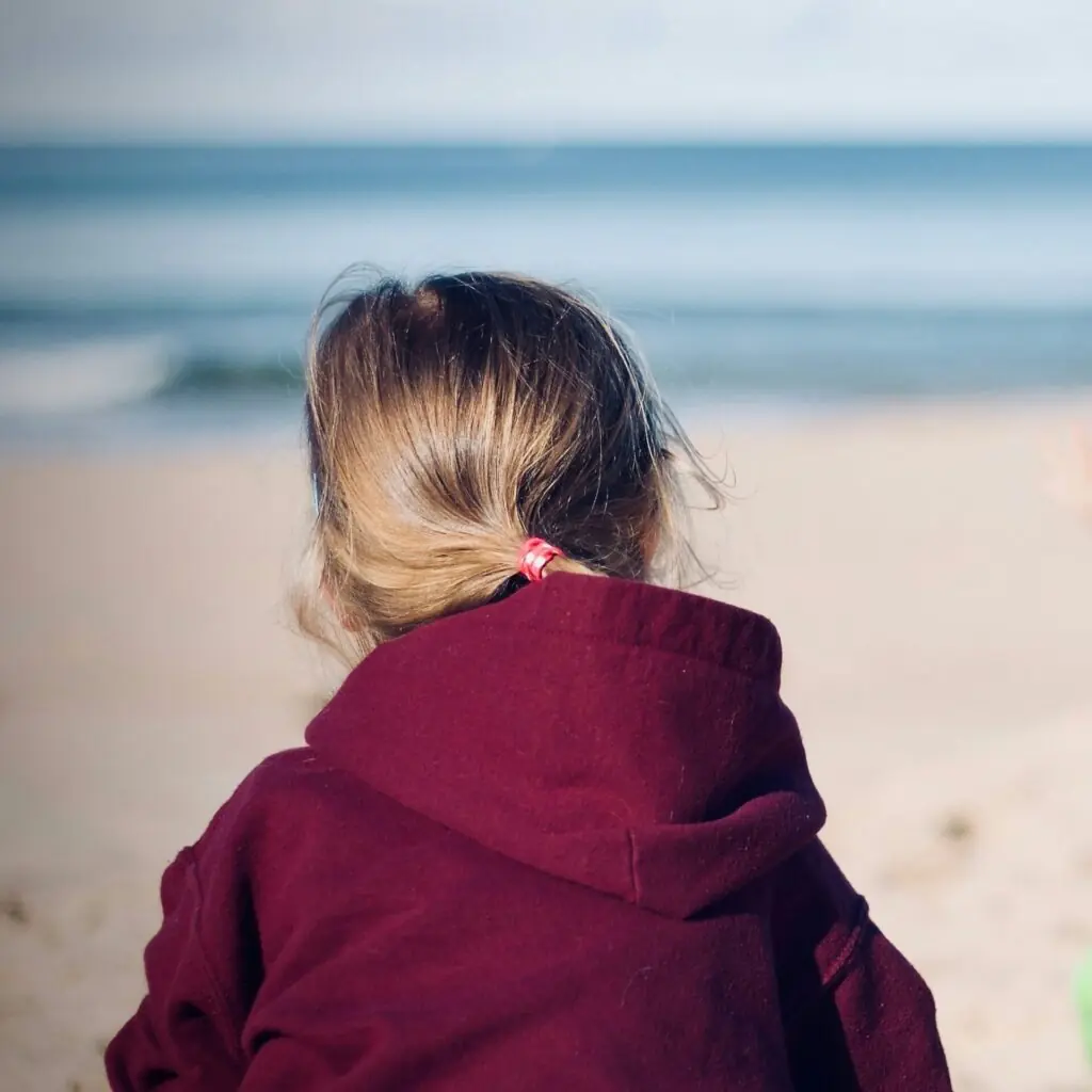 Child at the beach sits with back to camera
